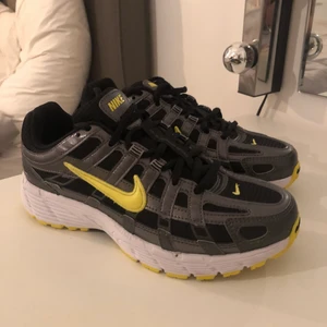 Nike skor st 37,5 - Det här är ett par oanvända nike sneakers i som är svarta med gula detaljer och vissa metallic/silvriga. Dom är i storlek 37,5 och är köpta på Footlocker.          Det är bara att buda på skorna och budgivningen startar på 600kr