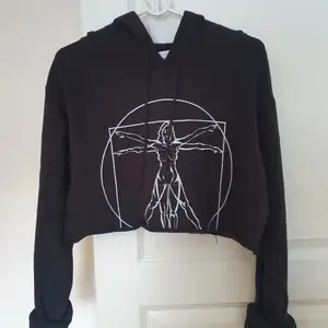 Svart croppad hoodie med trycket av Leonardo da Vinci's Vitruvanske mannen fast med en kvinna. Grymt häftig och aldrig använd! Endast testad. Storlek Medium. Inköp för flera flera år sedan på Na-kd och då var nypris 749kr.