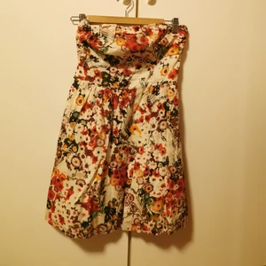 Blommig sommarklänning  - Jättefin blommig sommarklänning med smock bak. Söt liten rosett på ena sidan, men ett justerbart one-shoulder band (jättelätt att klippa bort om man vill). Skön i 100% bomull. Använd någon enstaka gång. Köparen står för frakten, men vet inte exakt kostnad nu. 