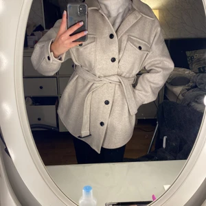 Jacka - En skjortjacka i en ljusgrå färg med svarta knappar och ett spänne fram till. Går även att knyta om man hellre vill det som på min bild. Inte använd mycket, gott skick!