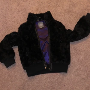 Svart fejkpäls jacka! - Denna as coola fejkpäls jacka är perfekt nu under våren! Innuti är den lila och super skön. Den har 2 fickor och kan stängas med dragkjedja! 