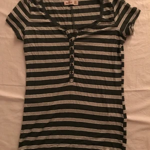 Randig Hollister T-shirt - Grå och vit randig Hollister T-shirt med knappar och vitt hollister märke längst ner strl XS i mycket bra skick💕