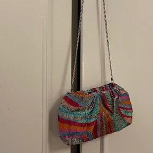 Färgglad festväska - Säljer denna otroliga väskan!! Nyligen inköpt och aldrig använd! Köpt på zalando men är i från märket parfois. Väskan har ett magnetlås och en tunn avtagbar silvrig kedja! Nypris: 349kr