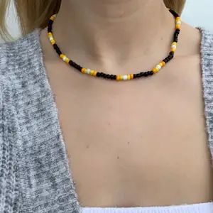Svart pärlhalsband med gula och orangea pärlor🖤🤍🧡💛 halsbandet försluts med lås och tråden är elastisk 