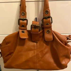Orange/brun-aktig vintage väska - Väska med mycket detaljer. Köpt second hand, i bra skick. Den är väldigt rymlig!! med tre stora fack med dragkedja till varje👍🏼