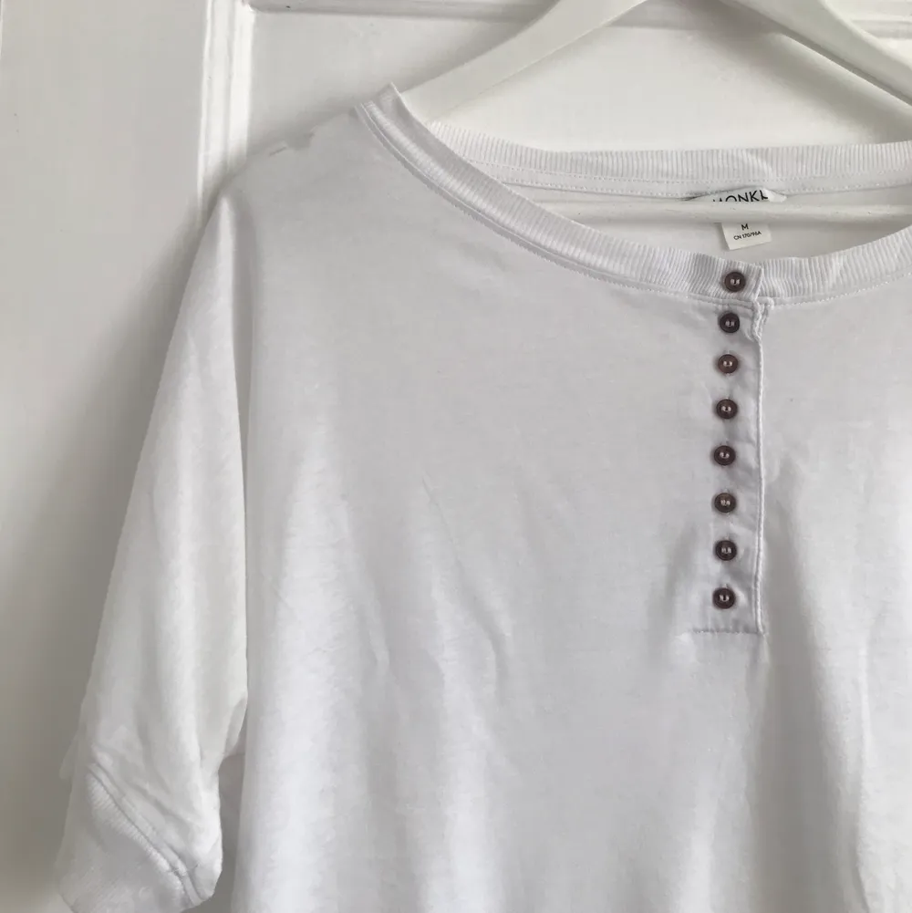En vit T-shirt med bruna små knappar som detalj framtill. Från Monki och i bra skick. Passar strl. M, L. . T-shirts.