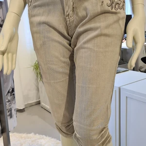 Jeans 5/8 dels längd - Stretching byxor i jeansmodell med fickor och hällor runt om. Detaljrika med sydda mönster och matchande stenar. Stentvättade i beige ton. Rynk veck sydda på sidorna av besluten. Slim fit  stl. 36
