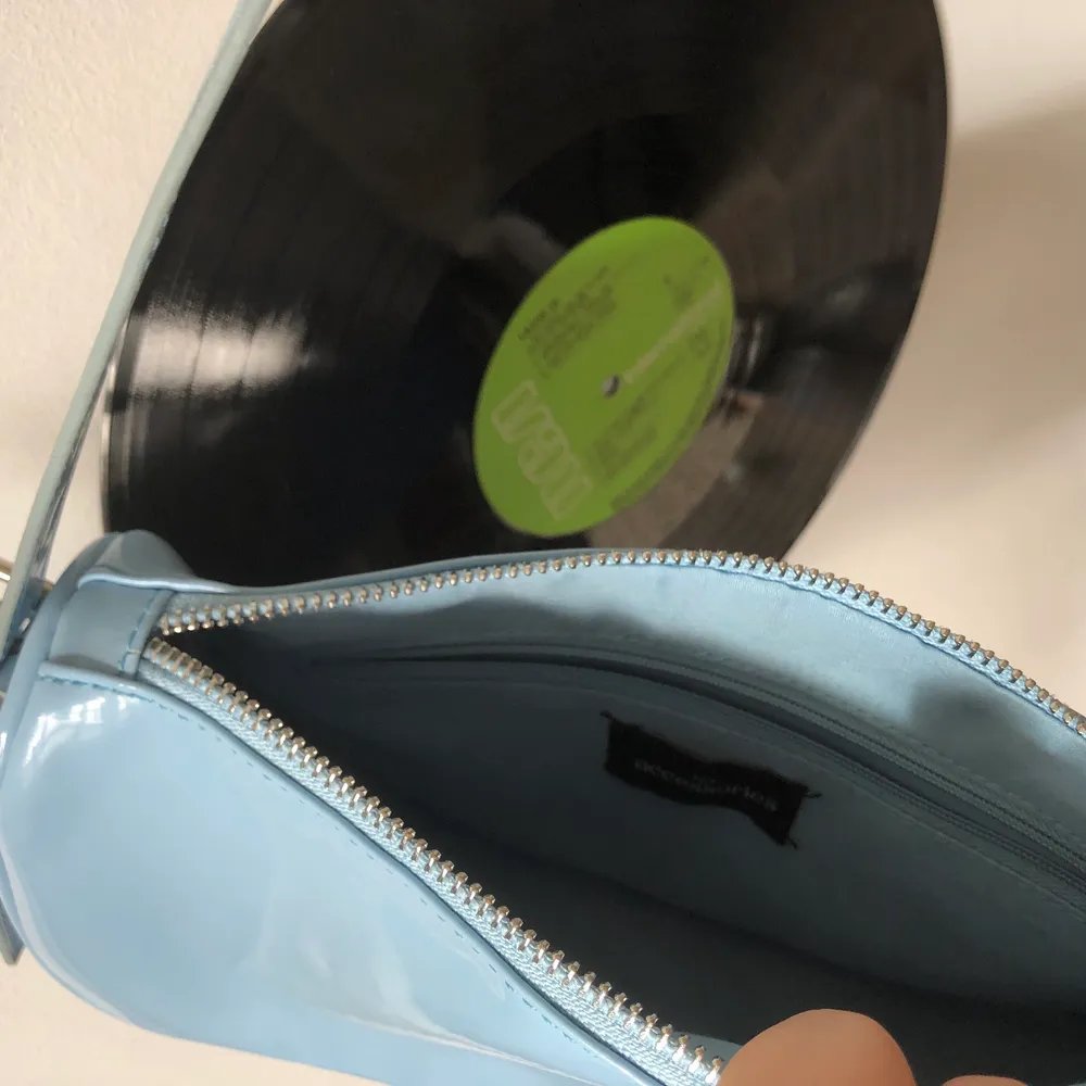 En babyblå vinyl baguettebag köpt från Nelly. Har en fläck (se bild 3)  som inte märks mycket alls om man inte kollar noga. Silvriga detaljer, dragkedja och har en ficka inuti. Skriv för fler bilder eller frågor!!!. Väskor.