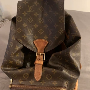 Louis Vuitton  MONTSOURIS  - Brun monogramduk och Golden Brass-hårdvara.  Ljus patina med fläckar. Canvas i bra skick.  Den har ett utvändig ficka med blixtlås på framsidan.  Läder pull -sträng stängning med lock topp för säkerhet, en interiör med ficka med blixtlås även där.  Mycket rymlig och stilren Mått: 30 * 35 * 12cm Väskan är välanvänd.   Sömmen har släppt på baksida undersida. (se bild)Detta går att lämnas in till en bra skinn skräddare för 1000 kr.  Inköpt på herr Judith 2017   Datum Kod  : MI 0030  (March 2000 in 