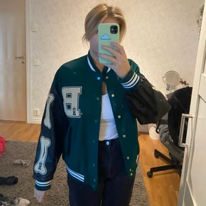Basketball jacka  - Basketball jacka grön med svarta armar av skinnimitation. Sitter fint oversized. Detaljer på armar samt bröst, lite tjockar så funkar bra till även kallare väder💚