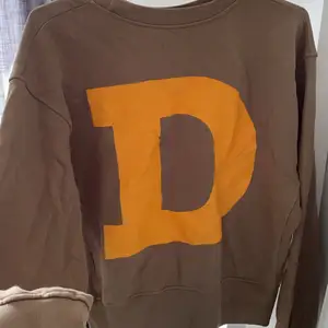 Brun sweatshirt med ett orange D på ryggen som en häftig detalj. Helt oanvänd😊