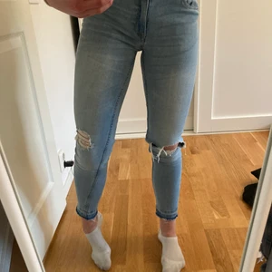Blå jeans med hål  - Blåa jeans i bra skick. Jeansen är i stretchigt material och har hål på båda knäna. 