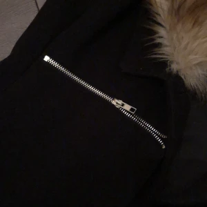 Kappa - Svart Kappa med snygga detaljer och avtagbar fuskpäls  i storlek xs från DM 