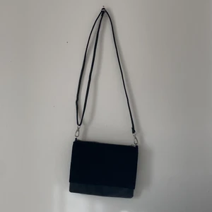 Praktisk svart axelremsväska från H&M - Svart axelremsväska i läder- och mockaimitation med silverdragkedja från H&M. Skjutsterbart och avtagbart axelband. Två öppningar, dragkedjan på den ena öppningen är något trög. Mått (ca): 23cm x 18cm. Hör av dig vid funderingar😃Köparen står för frakten!