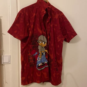 Skjorta med tryck - Röd skjorta med tryck. Två knappar borta längst ner. Inga fläckar eller hål. Skriv vid funderingar! 