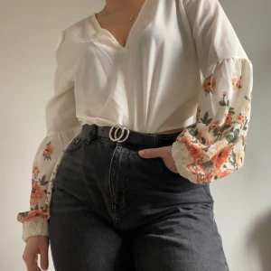 Blus med blommor - Fin vit blus med blommor på ärmarna. Har ett knyte fram men jag har använd den instoppad som på bilden. Storlek L men passar även mig som är S-M. Används tyvärr inte så den är i väldigt bra skick. Skriv ett meddelande för fler bilder eller frågor☀️