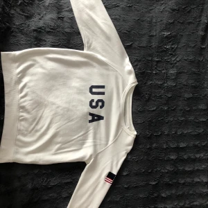 Sweatshirt  - En vit sweatshirt i storlek S. Använd 2 gånger. Har USA tryckt fram och USAs flagga på ena armen 