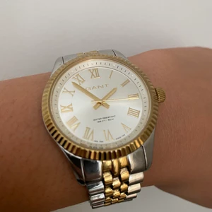 Gant klocka i guld och silver  - Klocka från märket Gant. Otroligt fin klocka men ligger bara och dammar hos mig. Den har en repa på glaset som syns i vissa ljus. Kvitton och extra länkar följa med. Behöver byta batteri! 💛 köptes för 2500:-