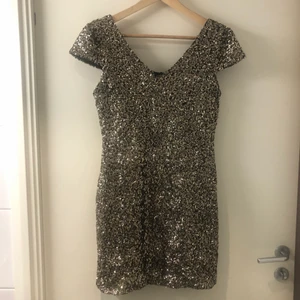 Guld svart paljett/ nyårsklänning - Paljettklänning från DM retro i gott skick. Inköpt för några år sedan men aldrig använd o bara hängt i garderoben. Storlek M, inte mycket men lite stretch.  Något figursydd och lite puffärmar.
