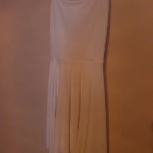Vit klänning - Snygg vid klänning med korsade band i ryggen, lite längre modell, fin till studenten. Säljes då den aldrig blivit använd, lapp finns kvar 