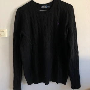 Svart kabelstickad Ralph Lauren medium - Svart kabelstickad från Ralph Lauren i 90% ull 10% kashmir, storlek medium med lila häst. Fint skick, inga hål eller dylikt.