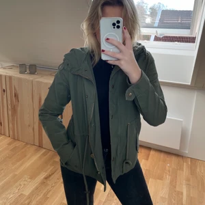 Grön jacka  - Grön tunn jacka som passar perfekt för hösten eller våren. Mycket detaljer, så som stor luva, dragsko i midja, dragkedja och knappar samt fickor. Använd fåtal gången så jackan är i väldigt bra skick. I storlek XS 