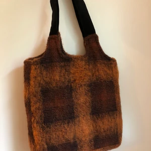 Väska, handväska - En väska jag älskar men aldrig använt. Fint oranget ginghammönster med luddig textur i ullblandat tyg, väskan är inte noppig. Handtaget är i mocka, riktigt löser enligt lapp. Insidan är simpel med nylon fordring i svart. Mig påminner väskan om något från unif.