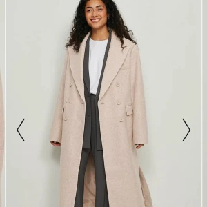 Oversize KAPPA från NAKD med splits  - Oversize beige kappa från NAKD med splits. Jättefin kappa som tyvärr passar inte mig i storlek, det är därför jag säljer den. Jag har bara testad den så det kommer skickas med lappen. Storlek 34 men lite oversize. Nypris på NKDA webbsidan 1000kr. Jag säljer den för 550kr. Köparen står för frakten. 