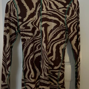 Ganni topp - Väldigt fin topp från ganni, sitter ”tajt” men inte oskönt, kort krage tyo halv polo. Den upplevs lite glittrig då de är små ”paljetter” på. 