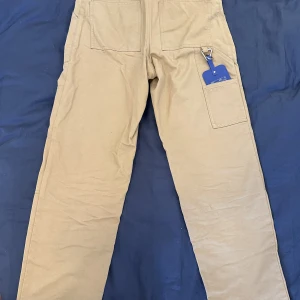 Arigato Iron Pants - Arigato byxor. Använda i väldigt bra skick. Små missfärgningar vid midjan, syns knappt och går förmodligen att bli av med om man stör sig på det. De är snyggare strukna😅Jag tror att nypris var 2200kr.