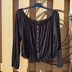 Svart topp  - Svart topp med lång ärm, bred hals, knappar fram, mudd nertill. 