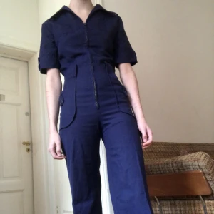 Byxdress 70-tal utsvängda ben - Byxdress från 70-talet för en ganska liten person!  Mått -  Armhåla till armhåla: 43cm, Midja: 64 cm, Innerbenslängd: 77,5cm