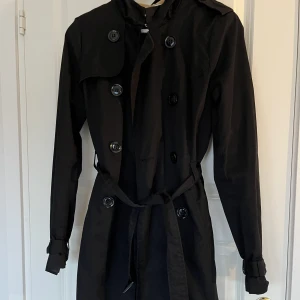 Svart lång trenchcoat  - Super söt svart trenchcoat med luva och rutigt tyg inuti Bra skick, inga defekter Skriv för bild på!!