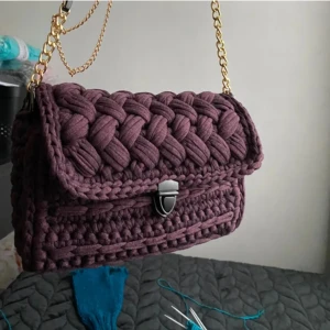 Väska - Djup lila väska gjord på bomullsgarn från modeindustrins rester. Har svarta detaljer och en guldkedja Mått: längd: 26cm, höjd: 18cm, djup:6cm PRIS: 900+porto