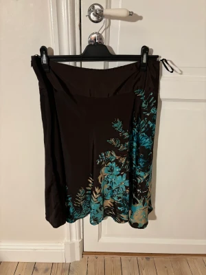 Lågmidjad kjol - Brun lågmidjad kjol från Vero Moda med blåa blommor. Passar bra i sommar och är i bra skick