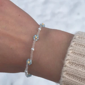 Pärlarmband med blommor  - Handgjort pärlarmband med ”seedbeads” och små akrylpärlor. Små, klara seedbeads och ljusblå blommor med gul mitt (eller vit). Kan förlängas med kedja utan extra kostnad. Finns även med guldfärgat lås. Perfekt julklapp!❤️