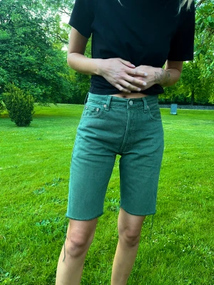 Levis shorts - Ett par gröna Levis shorts, lite lösare i modellen och längre i benen. Jag på bild har storlek 26 i midjan så skulle uppskatta storleken till 27-28 ungefär. Lappen säger 30 i midjan!  De är köpta secondhand innan men är i bra skick! 💚