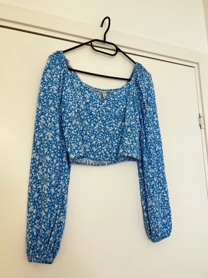 New yorker topp - Topp från New Yorker, ljusblå med vita blommor och fake knappar i fram. Stretchigt tyg i bak