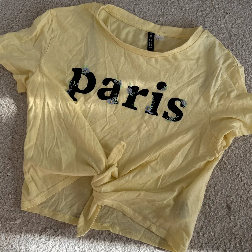 Gul t-shirt med Paris tryck över bröstet, knyt vid magen. T-shirts.