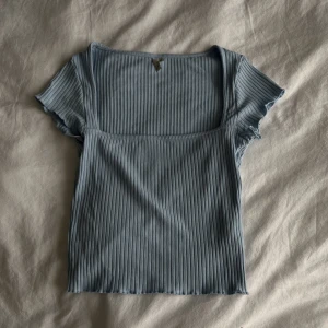 Babyblå topp - En blå topp med ”lettuce hem” och fyrkantig rak urringning. Sitter jättefint på och är lite stretchig.