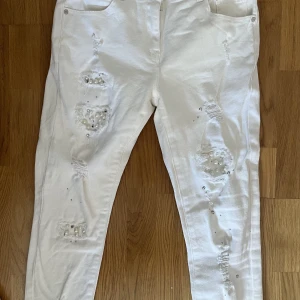 Jeans med pärlor  - Vita mid waist jeans med silvriga och vita pärlor på. Inga fläckar samt använda en gång. Säljer då dem är för korta i benen för mig. Jeansen är små i storleken 