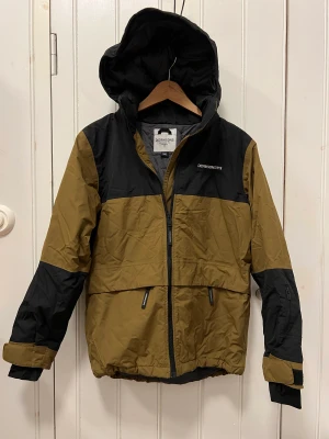 Didriksson vinterjacka stl 160 - Didriksson Theo BS JKT.  Vinterjacka från Didriksson. Mörkt olivgrön/svart.  Avtagbar luva, snölås, elastiska muddar med tumhål. Vattentät.  Som ny. Överstruket namn i lapp inuti jackan. 