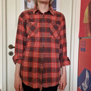 Rutig skjorta - Rutig skjorta i orange och brunt med vita och blåa inslag. Saknar 2 knappar på ena ärmen, men annars i fint skick!  Står ingen storlek men skulle säga att den är M.