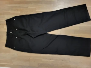 Oversized chino byxor - Thriftad chino byxor. Den har unika silver detaljer och är oversized. Kan fungera som kostym byxor också