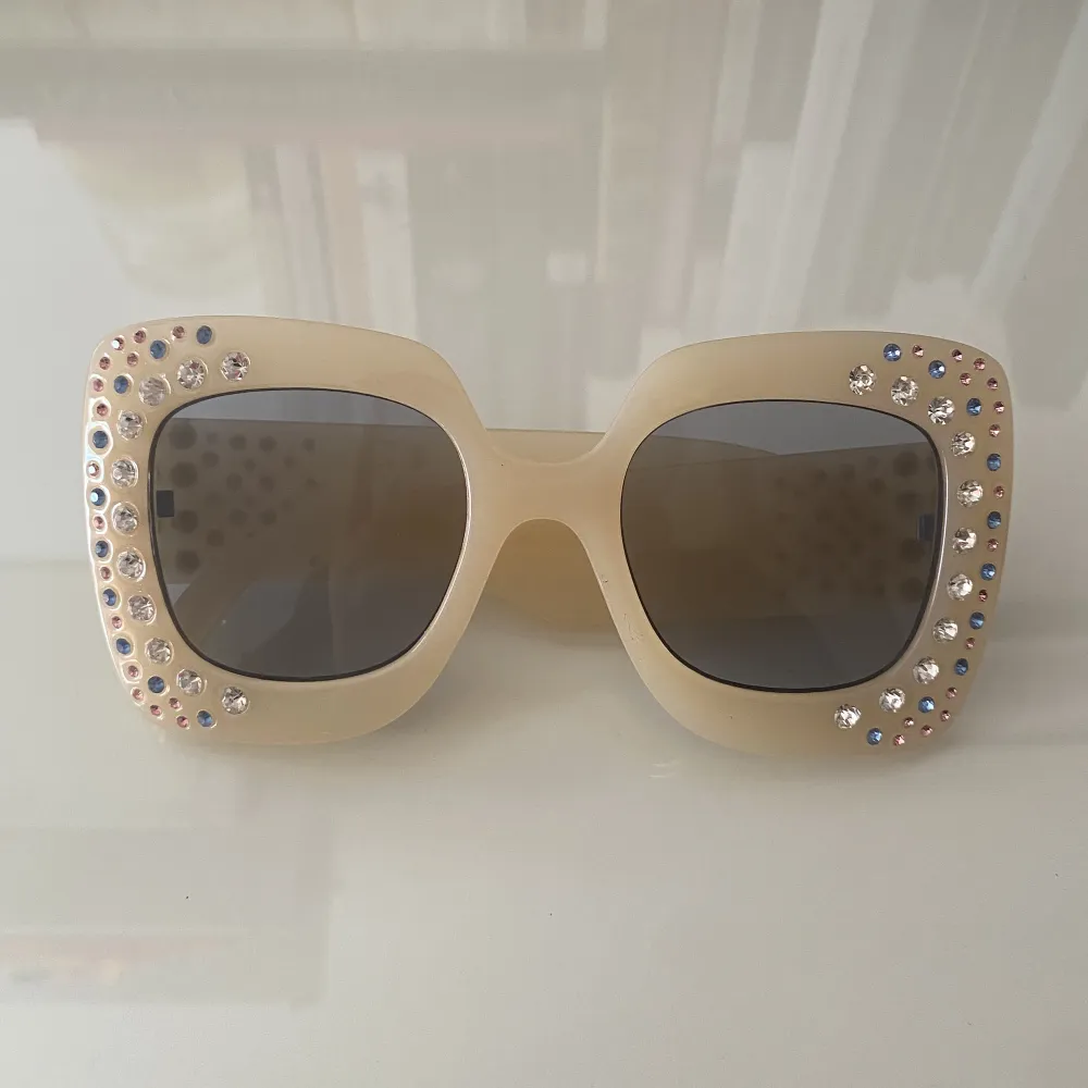 Krämvita oversizade solglasögon med med färgglada diamante stenar. Accessoarer.