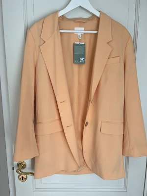 Orange kavaj - En fin orange kavaj från H&M. Aldrig använt, prislap sitter kvar. Sitter jätte fint, perfekt sommarkavaj. Storlek S.