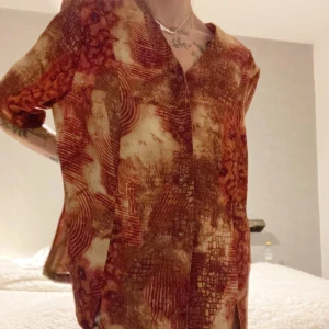 Blus 80-tal - Tunnt material med axelvaddar men inga stora liksom. Fint abstrakt mönster. Skickar gärna fler bilder, svårt att se för mycket finare irl. Knäpps med knappar fram