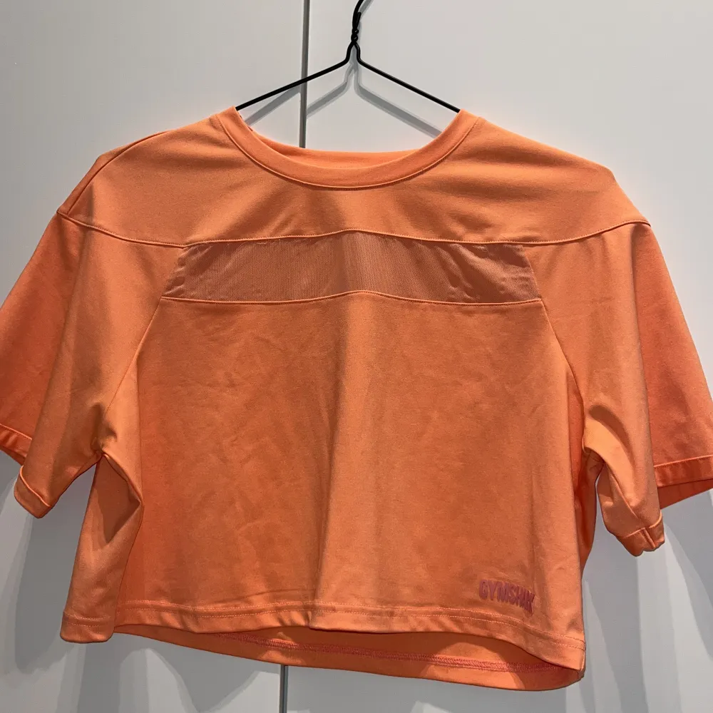 Träningströja från Gymshark, lite kortare modell. Skulle säga att färgen är en blandning av orange och rosa 🧡. T-shirts.