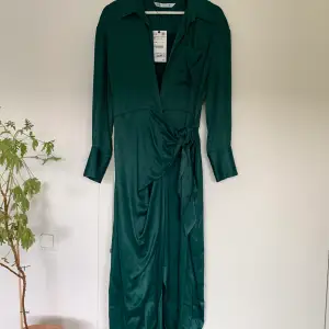Mörkgrön omlottklänning i satinmaterial från Zara. Storlek S men passar även M. Oanvänd med lappen kvar. Inköpt för 700 kr.   Hämtas i Uppsala eller skickas mot fraktkostnad.