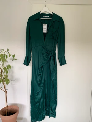 Lång omlottklänning Zara stl S - Mörkgrön omlottklänning i satinmaterial från Zara. Storlek S men passar även M. Oanvänd med lappen kvar. Inköpt för 700 kr.   Hämtas i Uppsala eller skickas mot fraktkostnad.